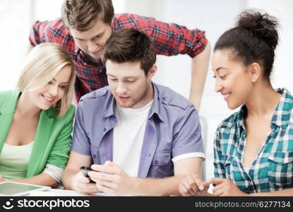 education, smatphones and internet - smiling students looking at smartphone at school