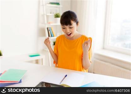 education, success, learning and people concept - happy smiling asian student girl with notebooks making fist pump gesture at home. asian student girl celebrating success at home