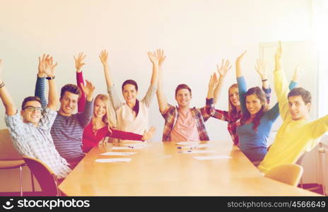 education, teamwork and people concept - group of smiling students raising hands in office