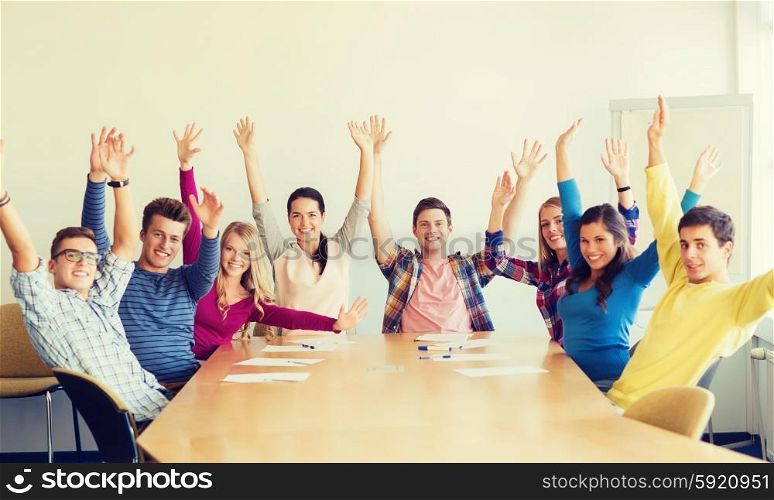 education, teamwork and people concept - group of smiling students raising hands in office