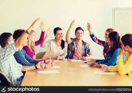 education, teamwork and people concept - group of smiling students with papers raising hands and voting indoors