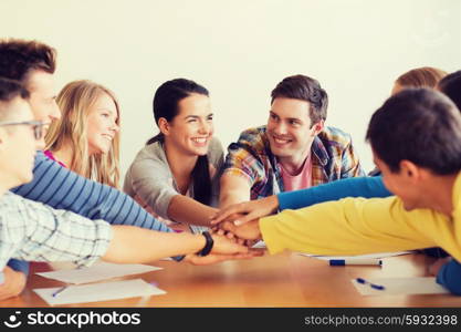 education, teamwork and people concept - smiling students with papers putting hands on top of each other