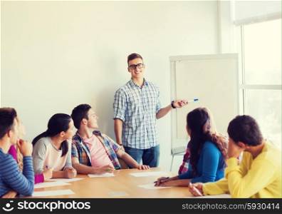 education, teamwork and people concept - smiling students with white board sitting an table indoors