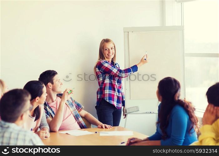 education, teamwork and people concept - smiling students with white board sitting an table indoors