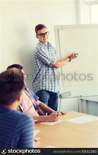 education, teamwork and people concept - smiling students with white board sitting at table indoors