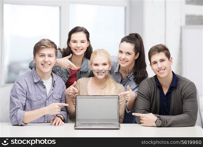 education, technology, advertisement and internet concept - group of smiling students pointing to blank black laptop screen