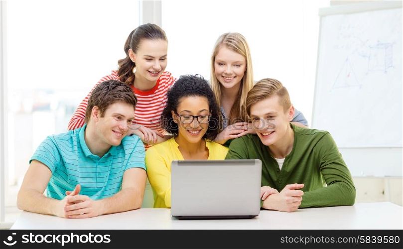 education, technology and college concept - five smiling students looking at laptop at school