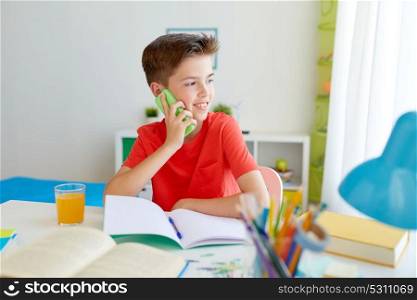 education, technology and communication concept - happy student boy distracting from homework and calling on smartphone at home. student boy calling on smartphone at home