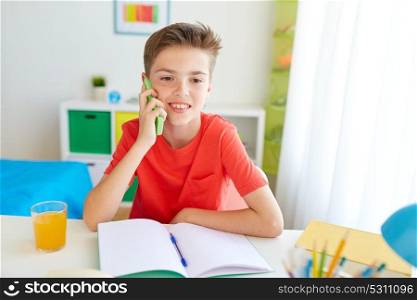 education, technology and communication concept - happy student boy distracting from homework and calling on smartphone at home. student boy calling on smartphone at home