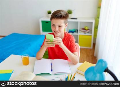 education, technology and communication concept - happy student boy distracting from homework and texting on smartphone at home. student boy with smartphone distracting from study
