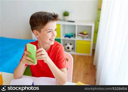 education, technology and communication concept - happy student boy with smartphone distracting from homework at home. student boy with smartphone distracting from study