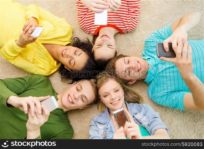 education, technology and happiness concept - group of young smiling people lying down on floor in circle with smartphones
