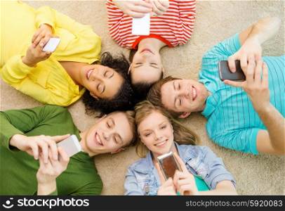 education, technology and happiness concept - group of young smiling people lying down on floor in circle with smartphones