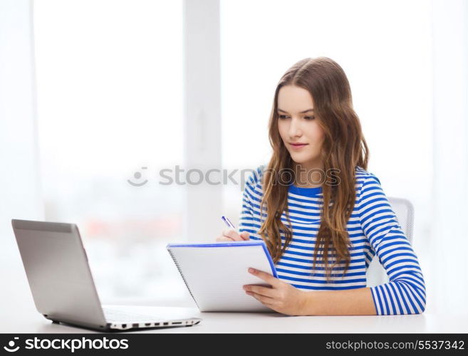 education, technology and home concept - concentrated teenage girl with laptop computer, notebook and pen at home