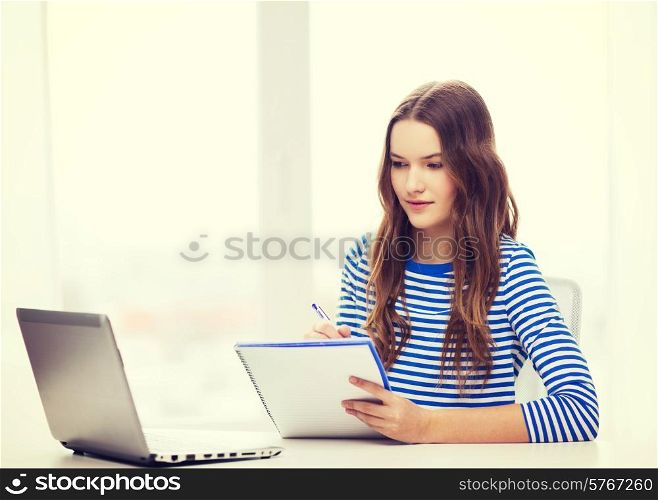 education, technology and home concept - concentrated teenage girl with laptop computer, notebook and pen at home