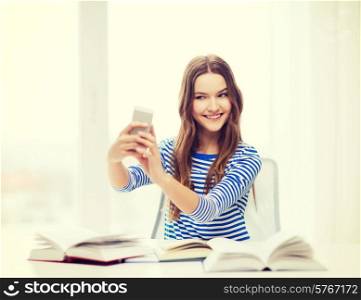 education, technology and home concept - happy smiling student girl with smartphone and books at home