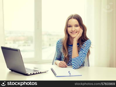 education, technology and home concept - smiling teenage girl with laptop computer, notebook and pen at home