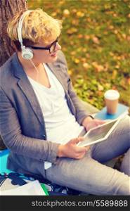 education, technology and internet concept - smiling male student in eyeglasses with tablet pc and headphones outdoors
