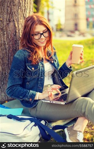 education, technology and internet concept - smiling redhead teenager in eyeglasses with laptop computer and take away coffee or tea