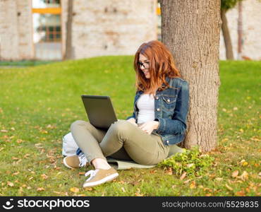 education, technology and internet concept - smiling redhead teenager in eyeglasses with laptop computer