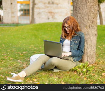 education, technology and internet concept - smiling redhead teenager in eyeglasses with laptop computer