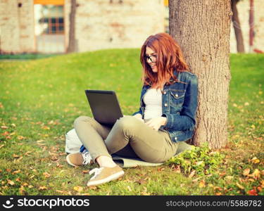 education, technology and internet concept - smiling redhead teenager in eyeglasses with laptop computer