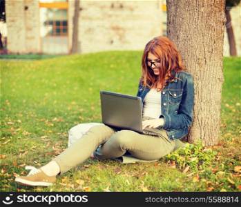 education, technology and internet concept - smiling redhead teenager in eyeglasses with laptop computer