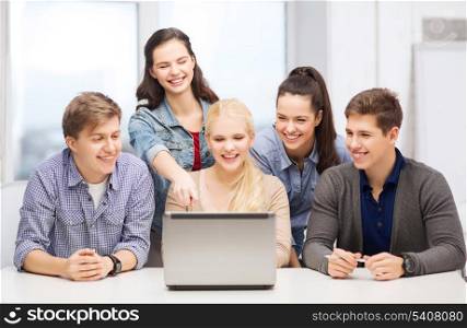 education, technology and internet concept - smiling students looking and pointing at laptop at school