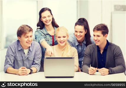 education, technology and internet concept - smiling students looking and pointing at laptop at school
