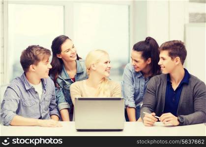 education, technology and internet concept - smiling students with laptop at school looking at each other