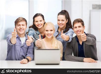 education, technology and internet concept - smiling students with laptop showing thumbs up at school