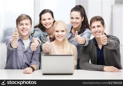 education, technology and internet concept - smiling students with laptop showing thumbs up at school
