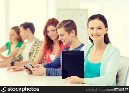 education, technology and internet concept - smiling teenage girl in front of students showing blank screen of tablet pc computer at school
