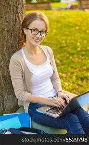 education, technology and internet concept - smiling teenager in eyeglasses with laptop computer, bag and notebooks