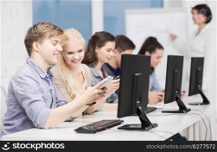 education, technology and internet concept - students with computer monitor and smartphones