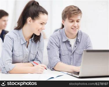 education, technology and internet concept - students with laptop and notebooks at school