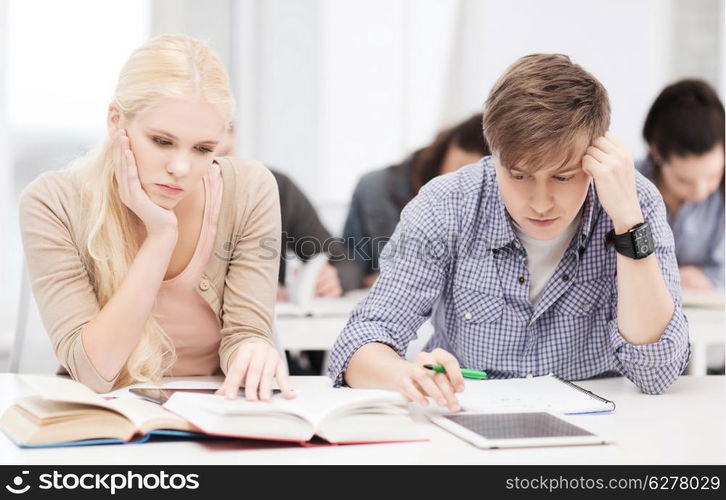 education, technology and internet concept - tired students with tablet pc, books and notebooks preparing for exam