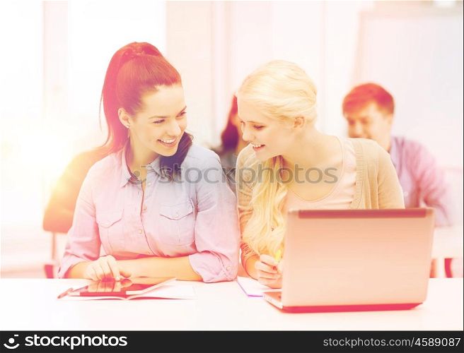 education, technology and internet concept - two smiling girl students with laptop, tablet pc and notebooks at school