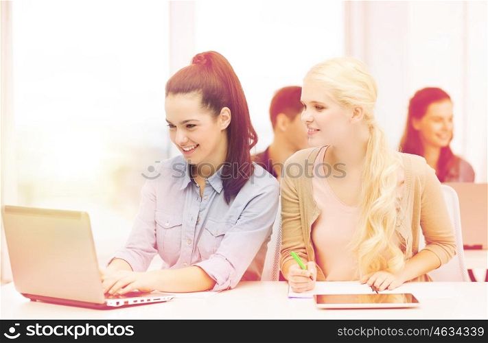 education, technology and internet concept - two smiling girl students with laptop, tablet pc and notebooks at school