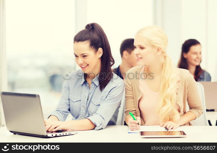 education, technology and internet concept - two smiling girl students with laptop, tablet pc and notebooks at school