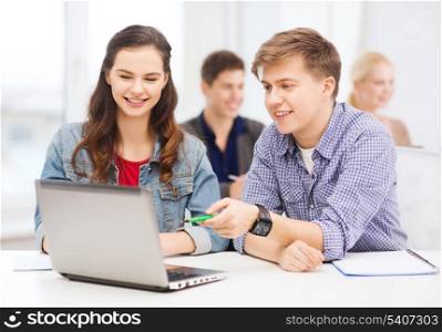 education, technology and internet concept - two smiling students with laptop and notebooks at school