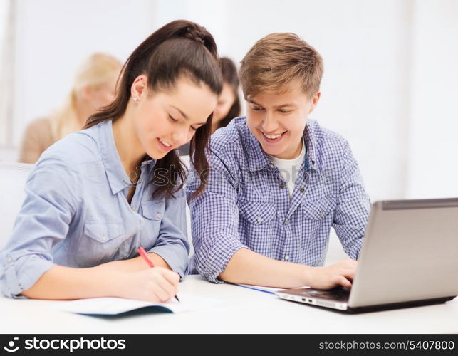 education, technology and internet concept - two smiling students with laptop and notebooks at school