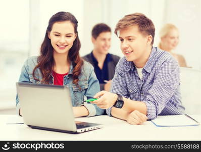 education, technology and internet concept - two smiling students with laptop and notebooks at school