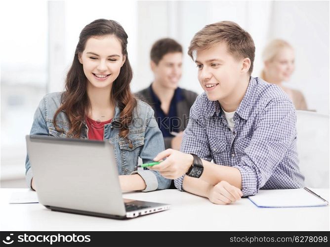 education, technology and internet concept - two smiling students with laptop and notebooks at school
