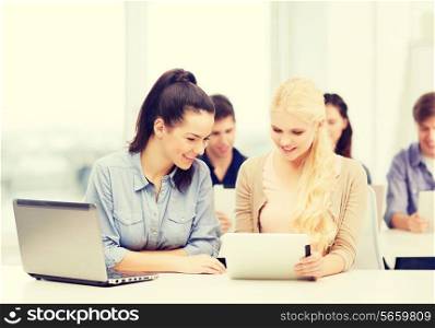 education, technology and internet concept - two smiling students with laptop computer, tablet pc and notebooks at school