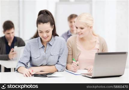 education, technology and internet concept - two smiling students with laptop computer, tablet pc and notebooks at school