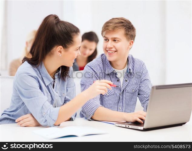 education, technology and internet concept - two smiling students with laptop computer and notebooks at school
