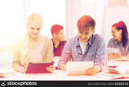 education, technology and internet concept - two smiling students with tablet pc, notebooks and books at school