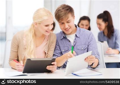 education, technology and internet concept - two smiling students with tablet pc and notebooks at school