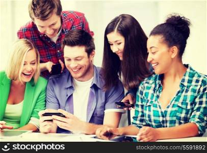 education, technology and internet - smiling students looking at smartphone at school